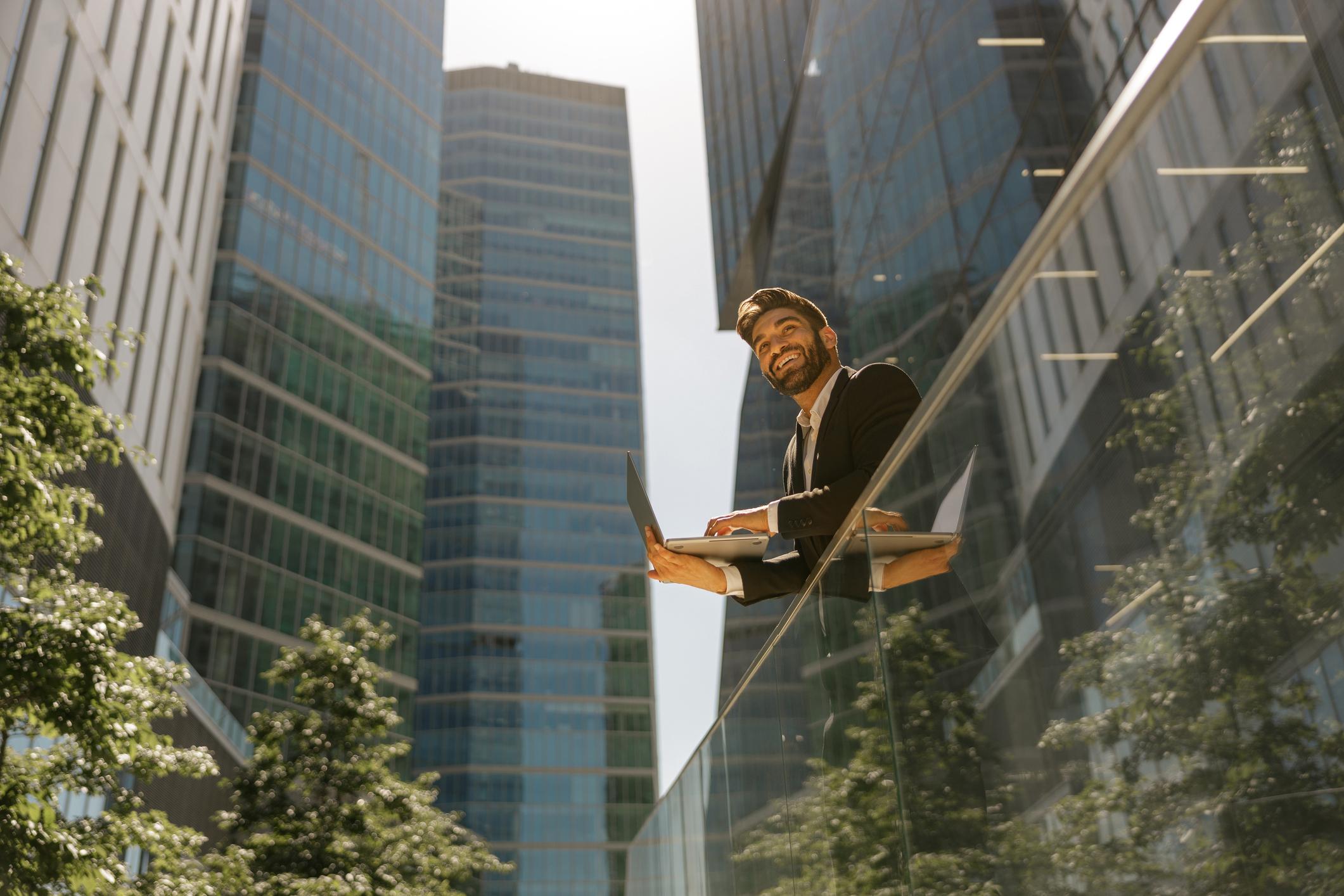 Man working on laptop standing on office terrace in the city.